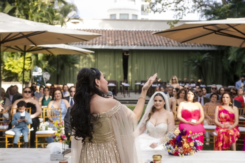 Sarai, de espaldas, alza la mano hacia los invitados y la novia durante la ceremonia