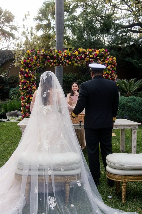 Los novios, de espaldas, frente a Sarai bajo el arco de flores